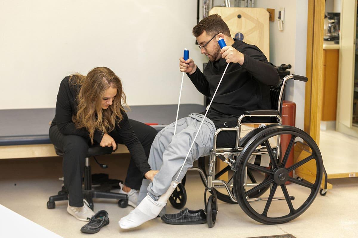 A student assesses the leg of another student who is sitting in a wheelchair